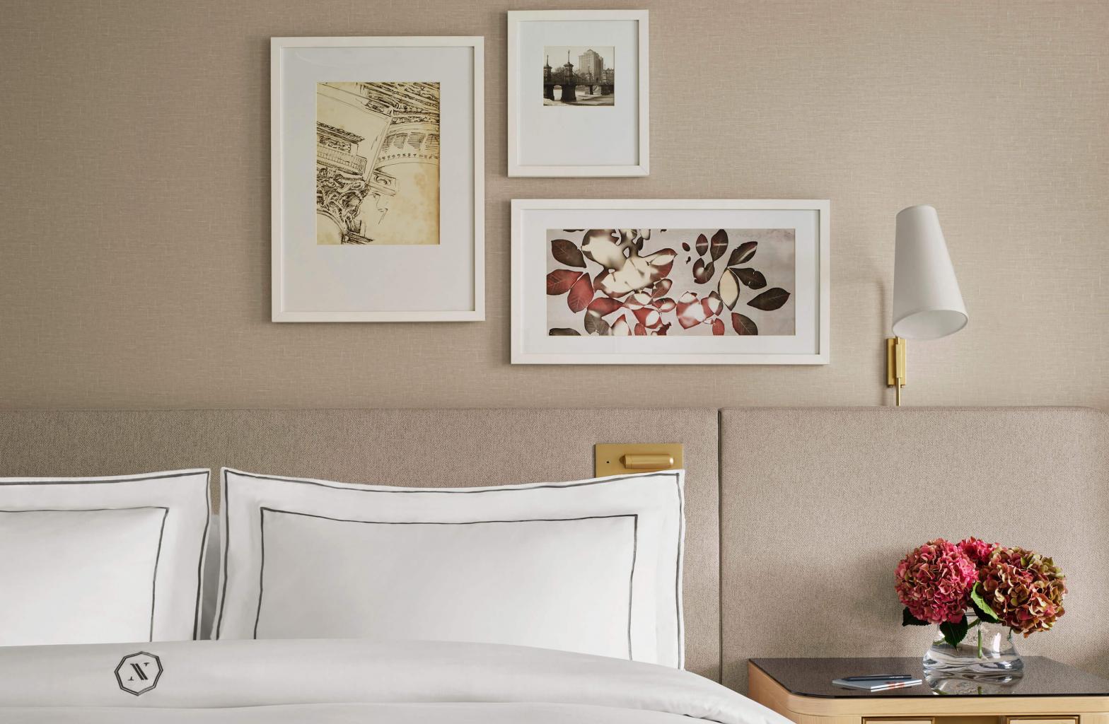 view of bed with crisp white sheets with three framed images on wall above it and flowers sitting on bedside table