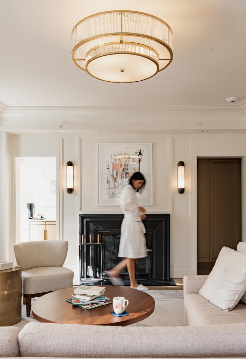 woman in robe and slippers walking in front of a fire place in hotel room 