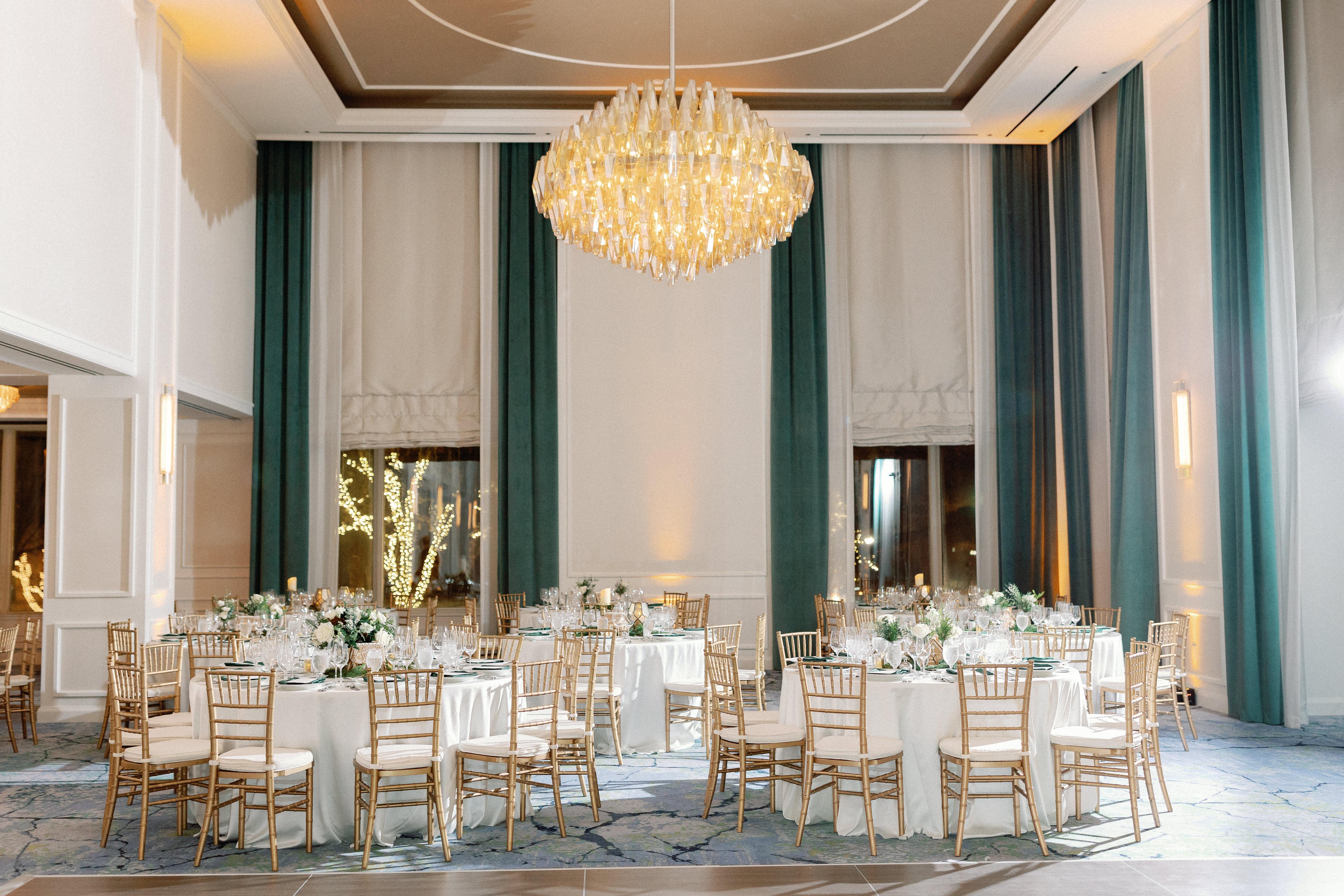Round tables setup for a wedding are positioned beneath a delicate crystal chandelier