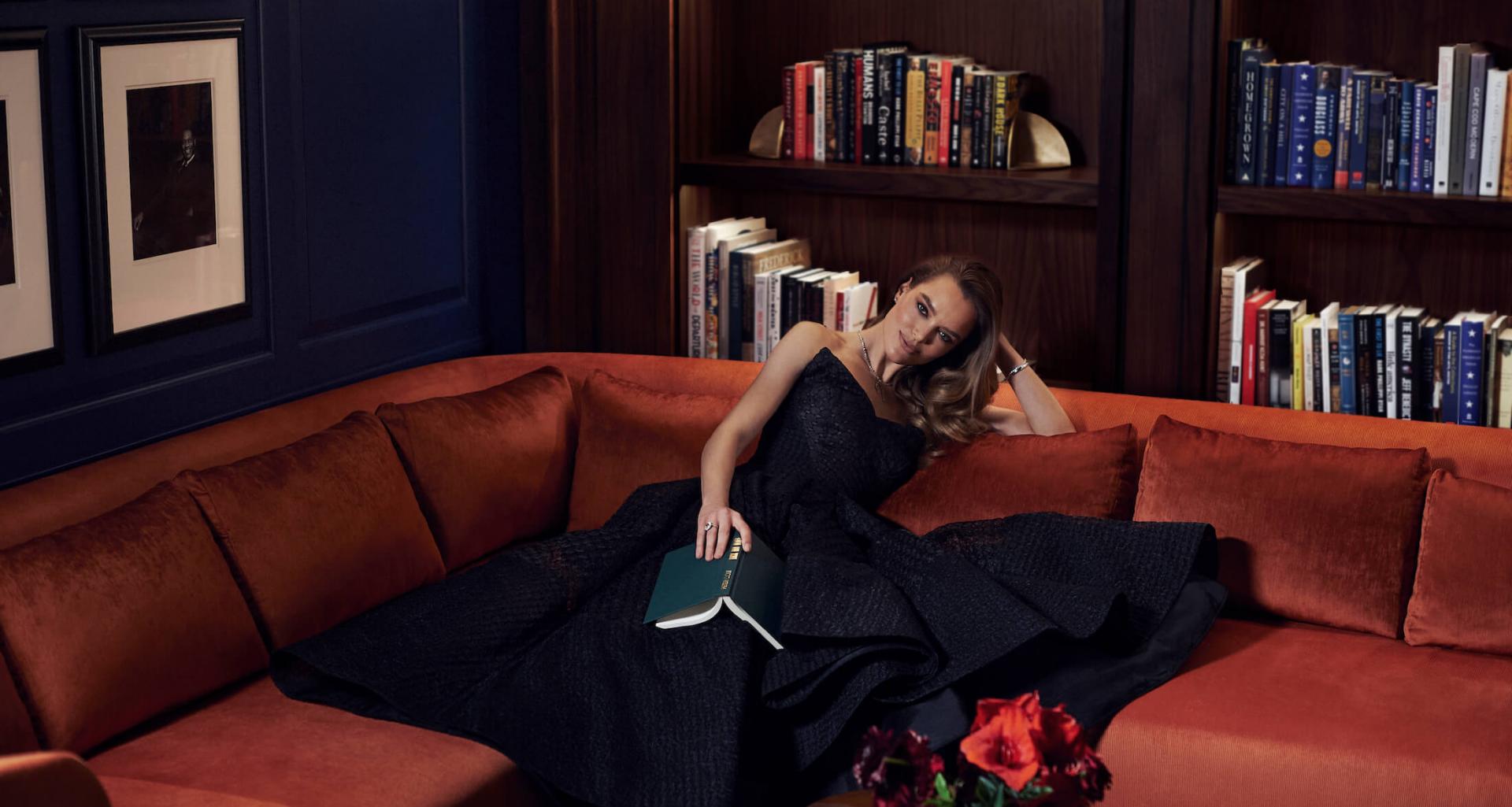 woman sits on corner coach in front of bookshelves
