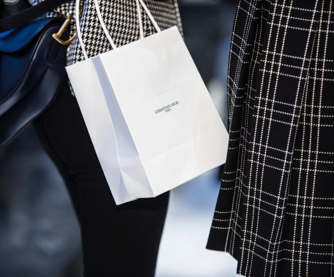 Two women standing, with one holding a Christian Dior bag.