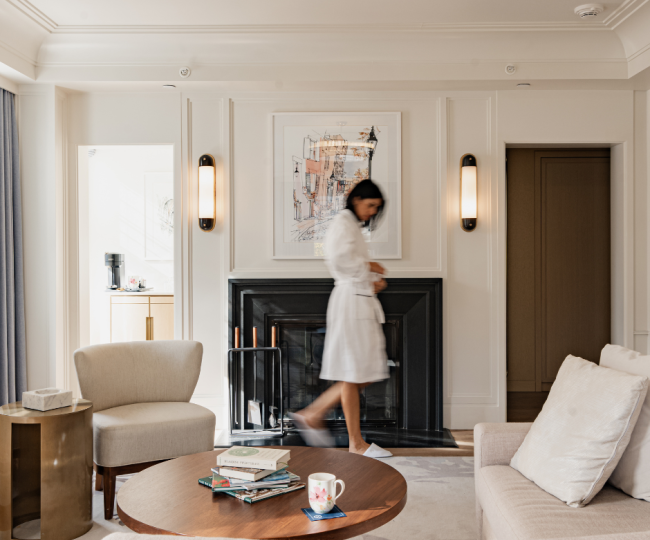 woman in robe and slippers walking in front of a fire place in hotel room 