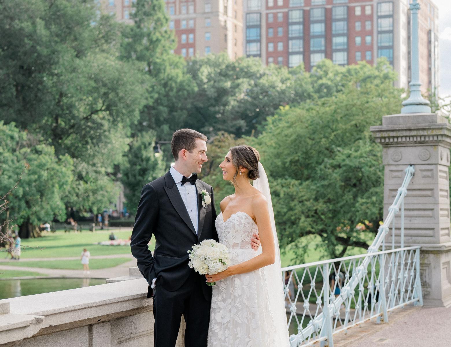 bride and groom standing on bridge in park in front of hotel 